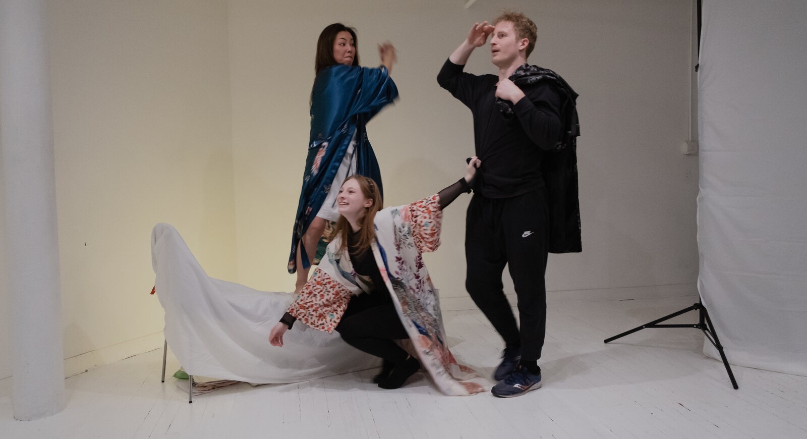 The ensemble in rehearsal, draped in silk robes, building the world of Mad Mystic in a white studio.