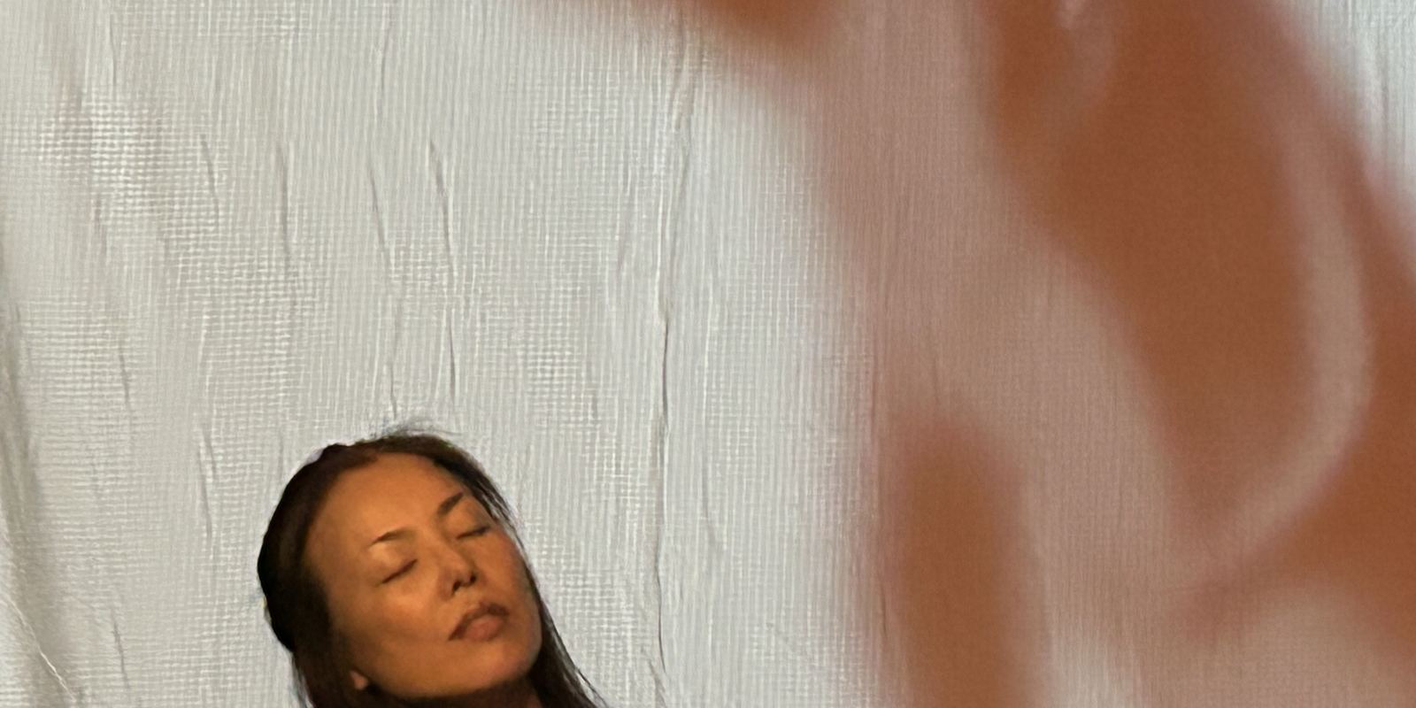 TomokoH DeblinGer on stage, eyes closed, with a large shadow looming behind her